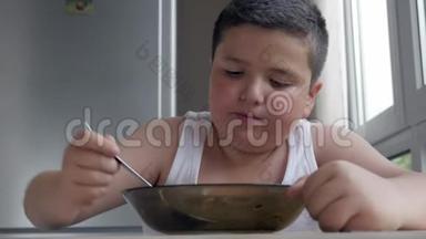 肖像小胖男孩坐在厨房里吃一勺汤，儿童肥胖问题
